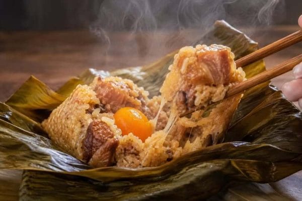 台湾ちまきの断面。塩漬け卵黄と大きな豚肉が入った熱々の台湾粽。もち米が伸びる食感と湯気が立つ様子。