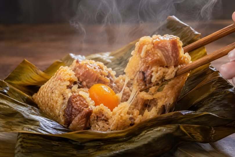台湾ちまきの断面。塩漬け卵黄と大きな豚肉が入った熱々の台湾粽。もち米が伸びる食感と湯気が立つ様子。