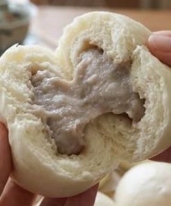 両手で半分に割ったホカホカのタロイモまんじゅう。中から自然な薄紫色のタロイモ餡があふれ、湯気が立ち上っている。背景には木のせいろと台湾茶器。